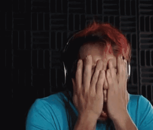a man with red hair wearing headphones is covering his face with his hands .