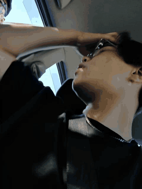 a man wearing glasses holds his hand to his forehead while sitting in a car