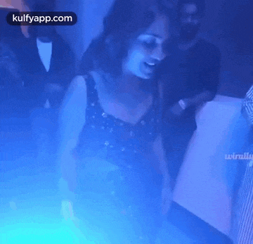 a woman in a black dress is dancing in a dark room with blue lights .