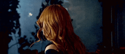 a woman with red hair is standing in front of a window with trees in the background .