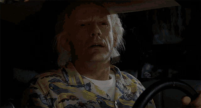 a man in a colorful shirt is driving a car at night
