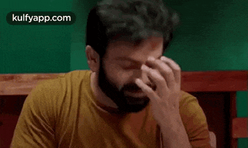 a man with a beard is sitting on a bed and holding his head .