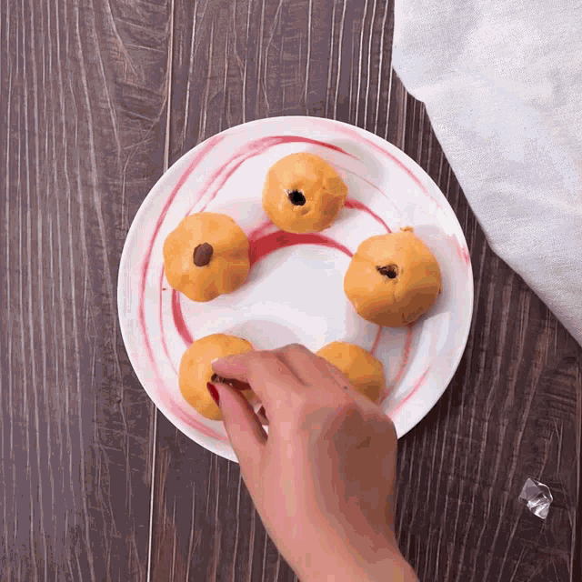 a white plate with a red swirl and a hand reaching for some food