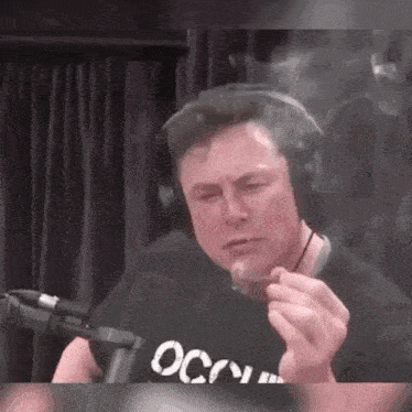 elon musk is smoking a cigarette while wearing headphones and a black shirt .