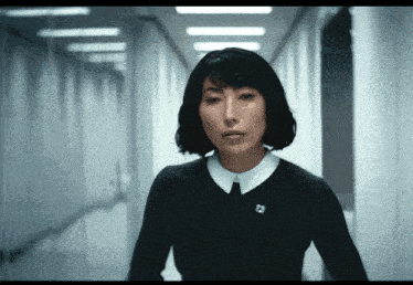 a woman wearing a black sweater and white collar has a pin on her collar that says a on it