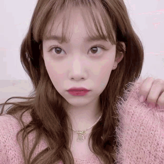 the girl is wearing a pink sweater and a necklace with the letter s on it .