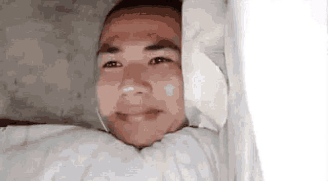 a man is laying in bed with a bandage on his head and smiling .