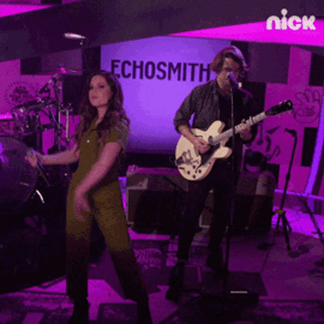 a man playing a guitar and a woman singing in front of a chosmith sign