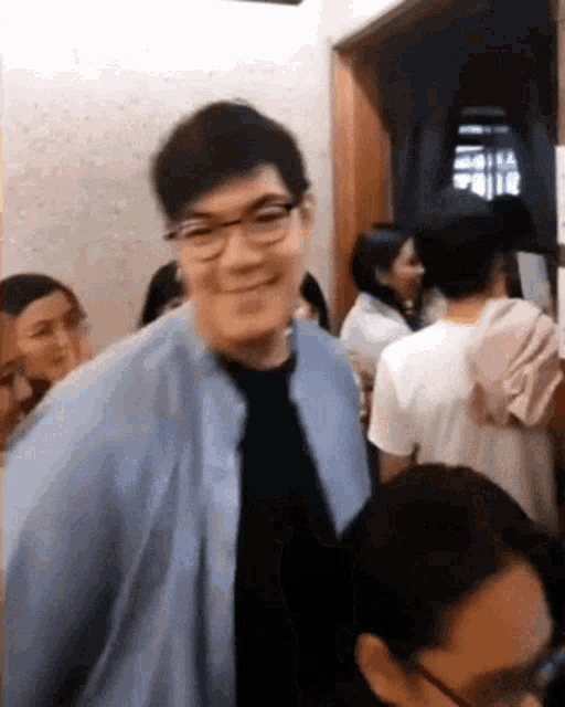 a man wearing glasses and a tie is smiling in front of a crowd of people
