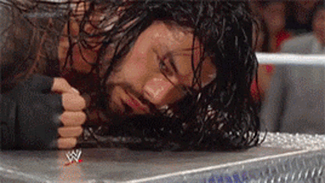 a wrestler is laying on the ground in a wrestling ring with his head on the ground .