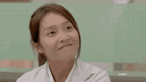 a woman in a white lab coat is smiling and making a funny face .