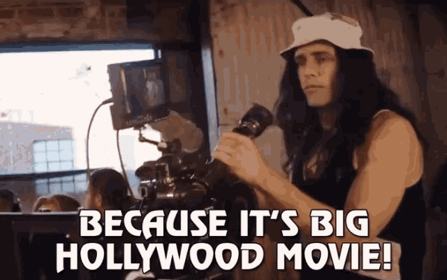 a man holding a camera with the words because it 's big hollywood movie
