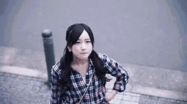 a young woman wearing a plaid shirt is standing on a sidewalk .