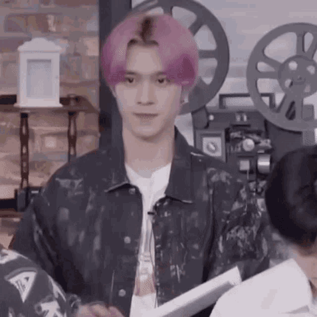 a young man with pink hair is standing in front of a camera .