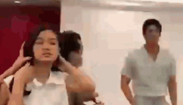 a man and a woman are standing next to each other in a room . the woman is adjusting her hair .