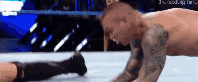 a man is laying on the ground in a wrestling ring while another man kicks him .