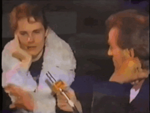 a man is holding a fork in front of another man who is holding a piece of food .