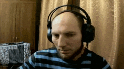 a bald man wearing headphones and a striped shirt looks at the camera