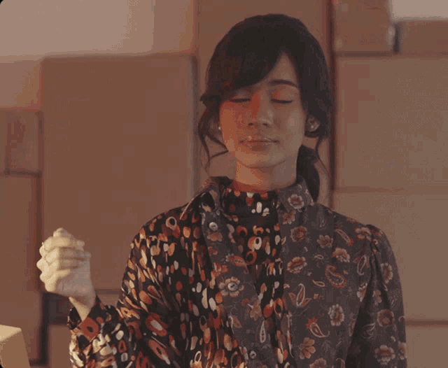a woman wearing a paisley shirt is standing in front of boxes