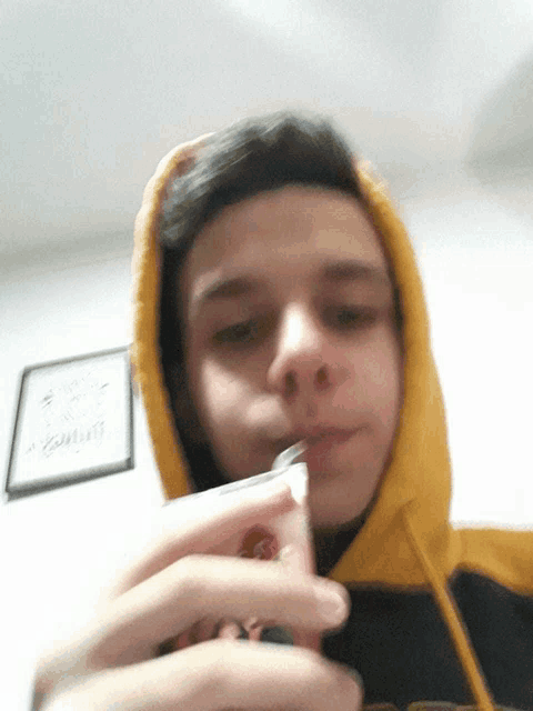 a young man wearing a yellow hoodie is holding a cigarette