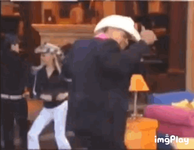 a man in a suit and cowboy hat is dancing with a woman in a living room .