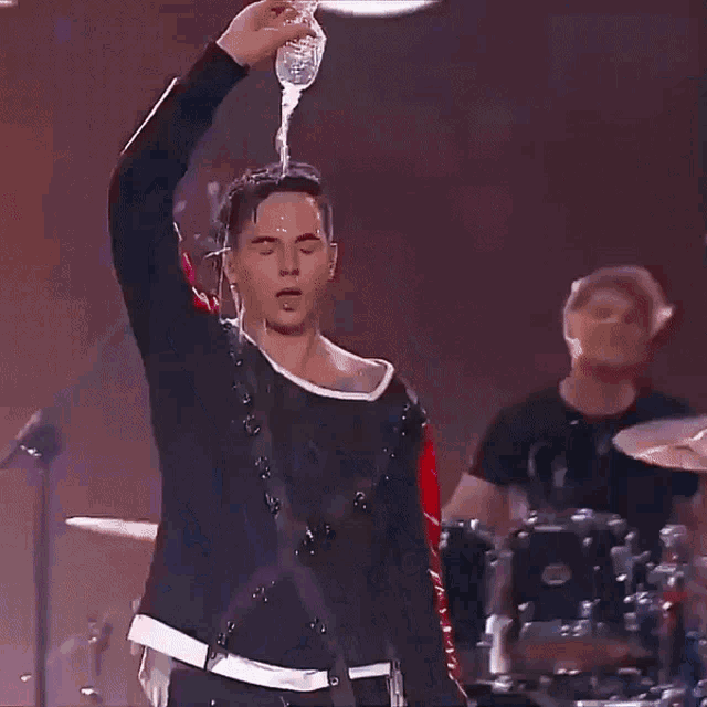 a man is pouring water on his head while playing drums .