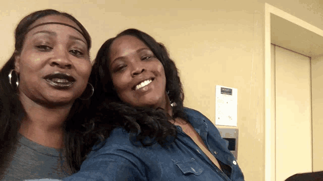 two women are posing for a picture in front of a wall that has a sign that says elevator