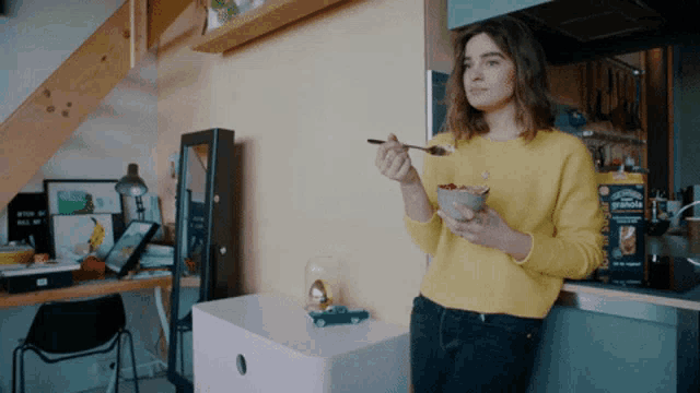 a woman in a yellow sweater is eating granola with a spoon