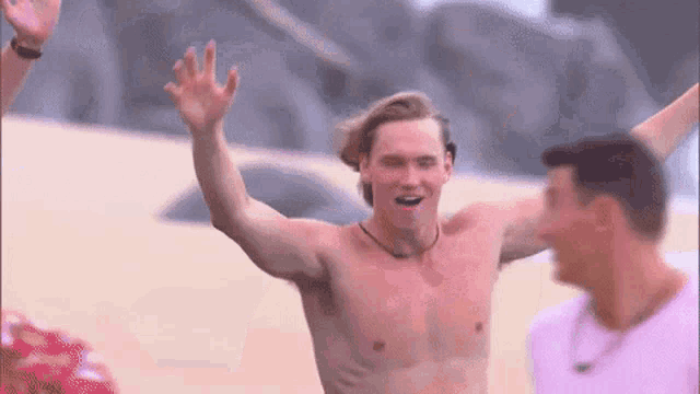 a shirtless man is waving his hands in the air while standing on a beach .
