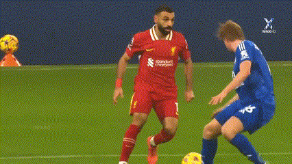 a soccer player in a red jersey is kicking a ball while another player in a blue jersey tries to stop him .