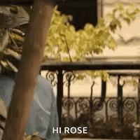 a man is standing on a balcony talking to a woman and says `` hi rose '' .