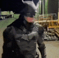 a man in a batman costume stands in a parking lot at night