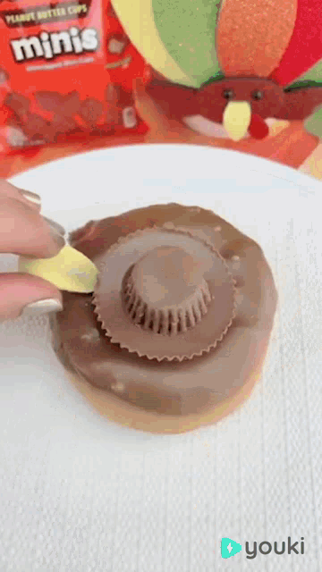 a person is putting a peanut butter cup on top of a chocolate donut .