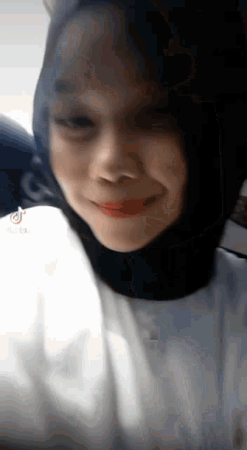 a woman wearing a hijab and a white shirt is smiling and looking at the camera .