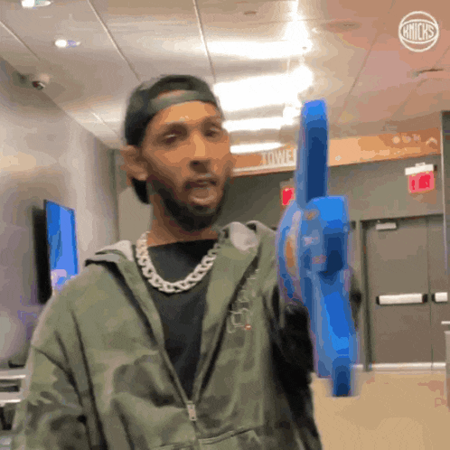 a man in a camo jacket holds a blue toy gun in a hallway
