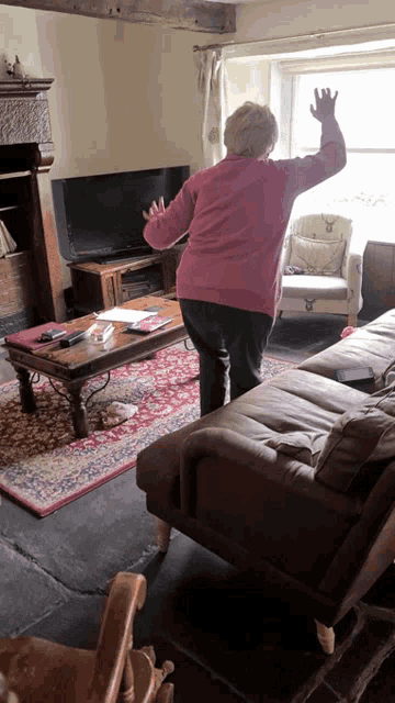 a woman in a pink sweater stands in a living room with her arms outstretched