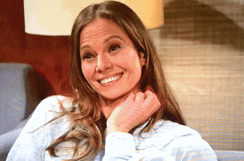 a woman with long hair is smiling and holding her hand to her chin