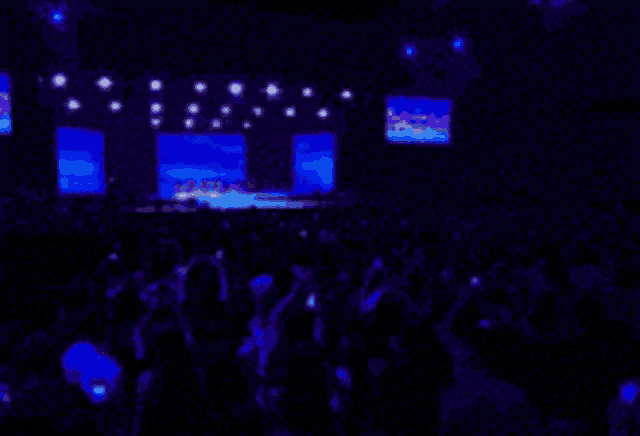 a blurred image of a crowd at a concert with a blue light behind them