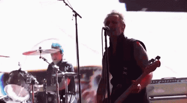 a man is playing a guitar and singing into a microphone while another man plays drums