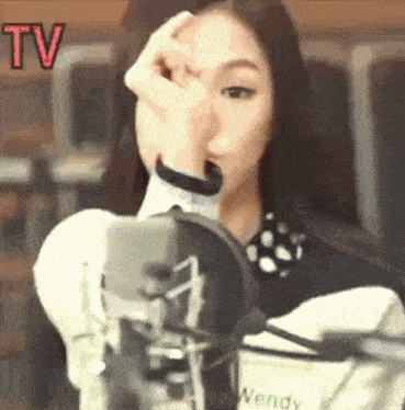 a woman is standing in front of a microphone covering her face with her hand .
