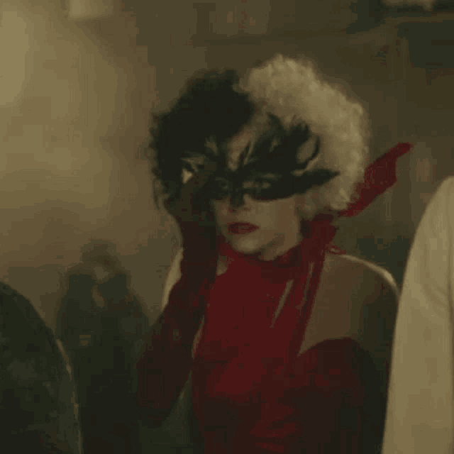 a woman wearing a red dress and a black mask is standing in a crowd .