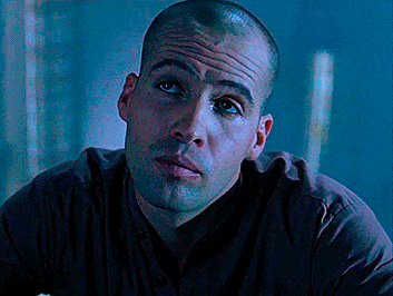 a man with a shaved head looks at the camera with a serious look on his face