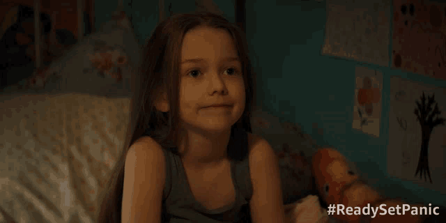 a little girl is sitting on a bed with #readysetpanic written in the corner