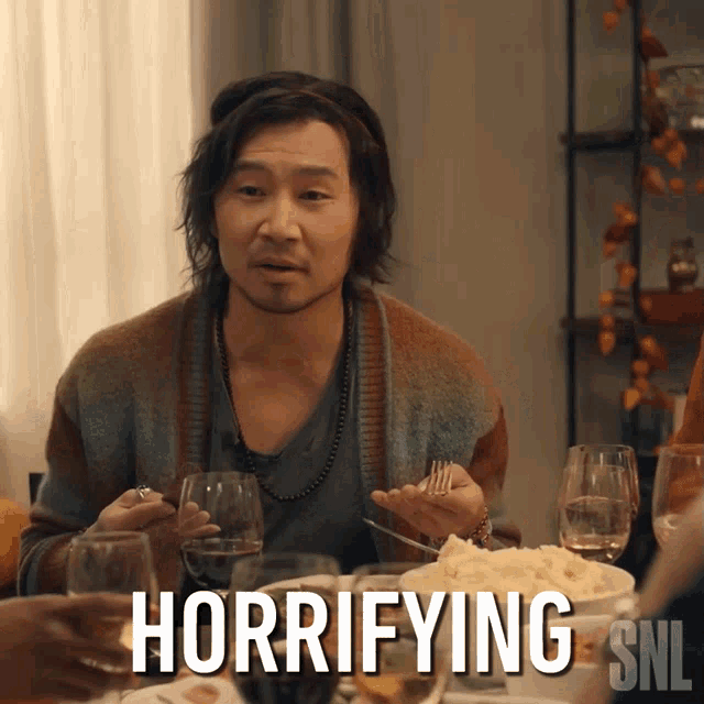 a man is sitting at a table with a plate of food and a sign that says " horifying snl "
