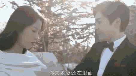 a man in a tuxedo and a woman in a white dress are standing next to each other in front of trees .