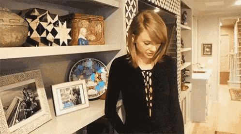 a woman in a black shirt is standing in front of a shelf filled with pictures .
