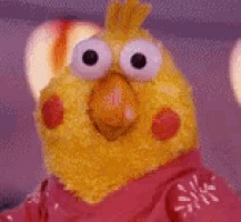 a yellow stuffed animal with big eyes and a red mouth is sitting on a bed .