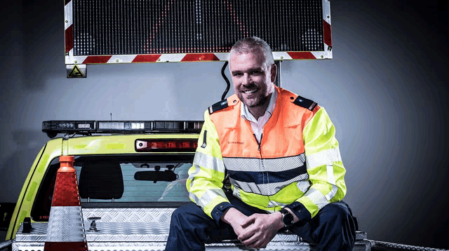 a man in a safety vest is sitting on the back of a vehicle