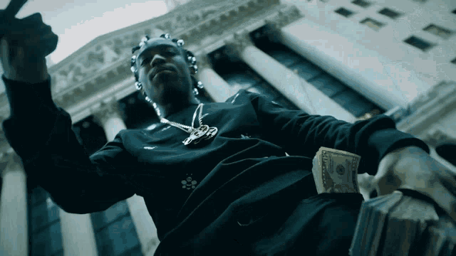 a man in a black shirt with the letter r on it is holding a stack of money