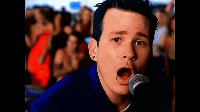 a man singing into a microphone with a crowd of people behind him